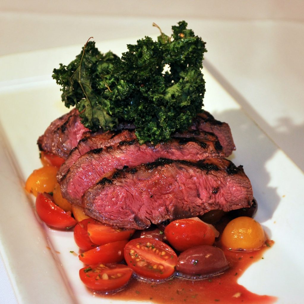 sliced meat with sliced tomatoes and green vegetable on white ceramic plate